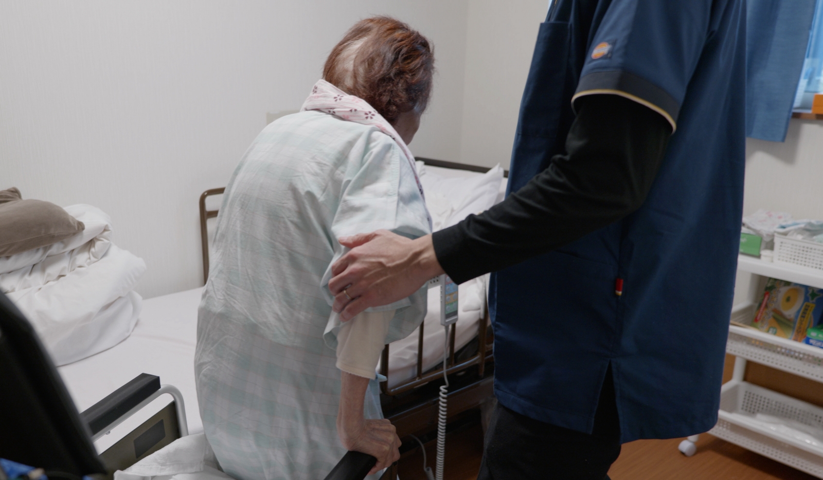 スタッフが高齢入居者の腰部をサポートしながら移動支援を行っている様子